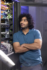 Smiling IT technician standing with arms crossed in server room at industry - FKF04688