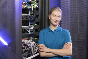 Blond IT trainee standing with arms crossed in server room at industry - FKF04690