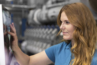 Blond IT technician using touch screen device in factory - FKF04695