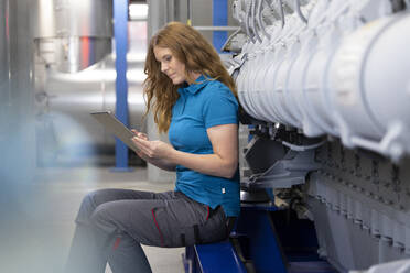 Blonder Techniker mit Tablet-PC in der Fabrik sitzend - FKF04699