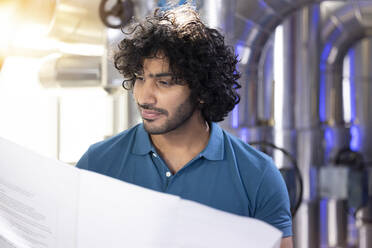 Technician examining blueprint standing in factory - FKF04702