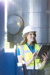 Technician wearing hardhat holding tablet PC standing in industry - FKF04729
