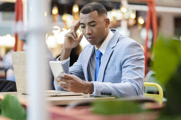 Businessman using smart phone sitting with laptop at sidewalk cafe - JCCMF05639