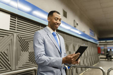 Smiling businessman using table PC at train station - JCCMF05665