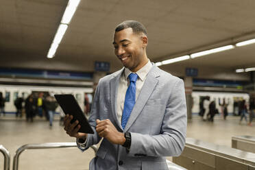 Happy businessman using tablet PC at train station - JCCMF05667