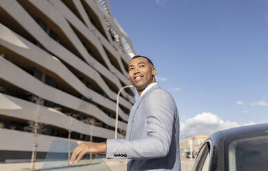 Smiling businessman standing by car on sunny day - JCCMF05684