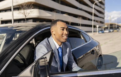 Smiling businessman sitting in car on sunny day - JCCMF05686