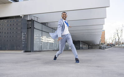 Smiling businessman dancing in front of building - JCCMF05688