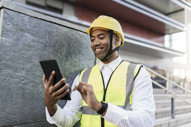 Smiling engineer using tablet PC standing by wall - JCCMF05709