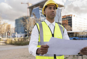 Engineer holding blueprint working at construction site - JCCMF05715