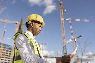 Ingenieur, der auf einer Baustelle an einem sonnigen Tag einen Bauplan liest - JCCMF05717