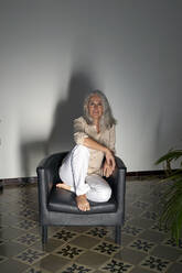 Lächelnde Frau, die zu Hause auf einem Sessel sitzt - VEGF05406