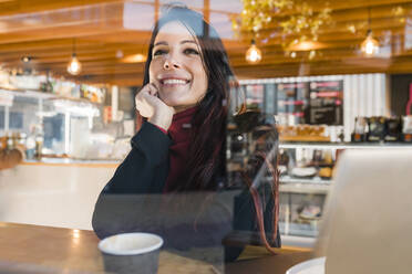 Nachdenkliche Geschäftsfrau mit Hand am Kinn durch das Glas eines Cafés gesehen - JRVF02880