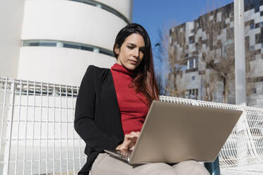 Geschäftsfrau mit Laptop auf einer Bank sitzend - JRVF02882