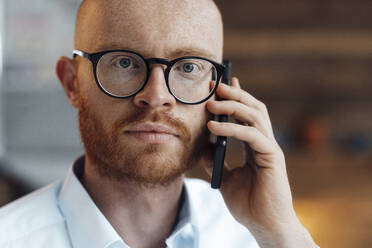 Businessman wearing eyeglasses talking on mobile phone - JOSEF07593