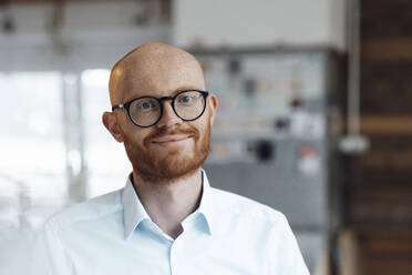 Smiling young bald working man wearing eyeglasses in office - JOSEF07596