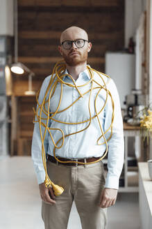 Young businessman covered with cable standing in office - JOSEF07597