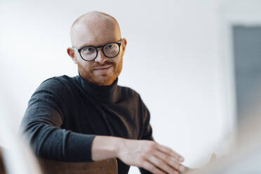 Smiling working man wearing eyeglasses sitting in office - JOSEF07617