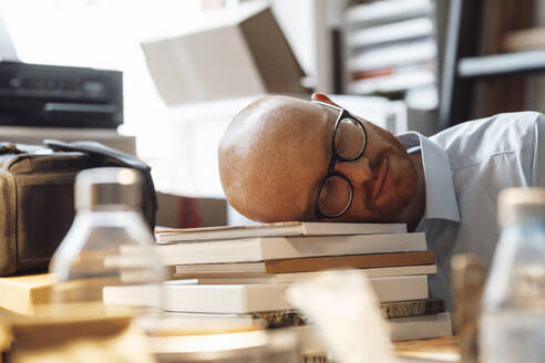 Tired businessman sleeping on books in office - JOSEF07659