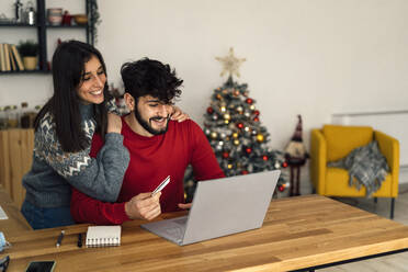 Happy couple doing online shopping through laptop at home - GIOF14931