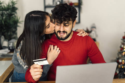 Junge Frau küsst die Wange ihres Freundes beim Online-Shopping mit dem Laptop zu Hause - GIOF14932