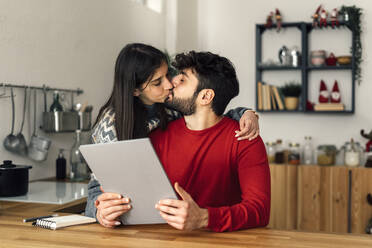 Man holding tablet PC kissing girlfriend in kitchen at home - GIOF14938