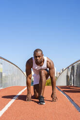 Sportsman kneeling on running track on sunny day - DLTSF02813