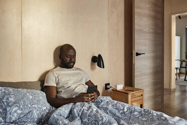 Young man using smart phone in bedroom at home - DSHF00140