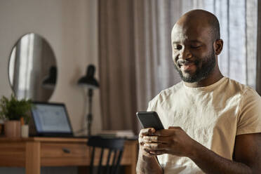 Smiling man using smart phone at home - DSHF00144