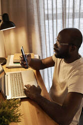 Geschäftsmann bei der Arbeit im Home-Office mit Textnachrichten über sein Smartphone - DSHF00148
