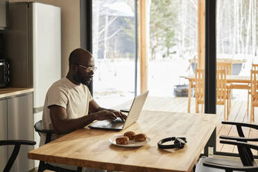 Young man using laptop at table in kitchen at home - DSHF00150