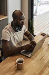 Mann benutzt Laptop auf Tisch neben Teetasse zu Hause - DSHF00152