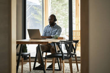 Businessman using laptop on dining table at home - DSHF00166