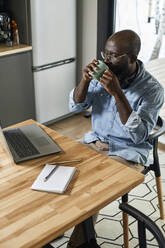 Geschäftsmann trinkt Tee und schaut auf den Laptop am Esstisch zu Hause - DSHF00170