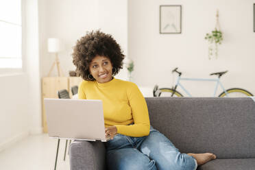 Lächelnde Frau mit Laptop auf dem Sofa im Wohnzimmer sitzend - JCZF00975