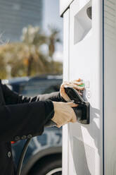 Frau beim Einstecken des Ladegeräts für Elektroautos an der Ladestation - GMCF00248