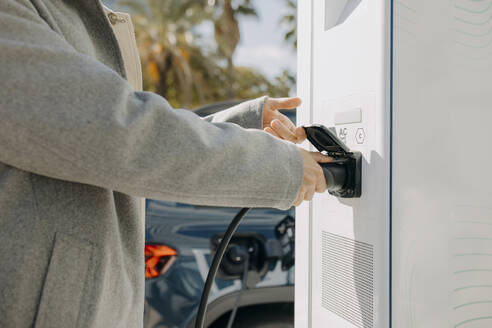 Hand on man plugging car charger at station - GMCF00259