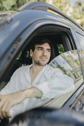 Junger Mann schaut aus dem Fenster eines Elektroautos - GMCF00261