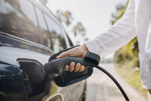 Hand eines Mannes, der ein Elektroauto am Straßenrand eines Bahnhofs auflädt - GMCF00271