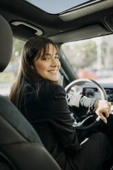 Smiling businesswoman sitting inside electric car - GMCF00276