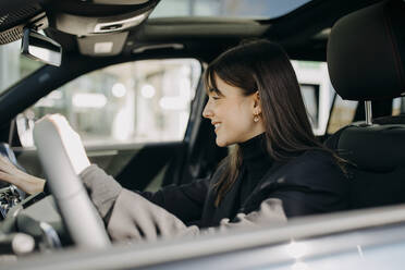 Lächelnde Geschäftsfrau mit dem Bedienfeld eines Elektroautos - GMCF00277