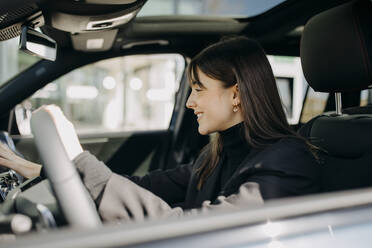 Smiling businesswoman using control panel of electric car - GMCF00277
