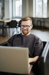 Happy businessman working on laptop at office - DSHF00209