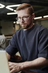 Concentrated businessman with eyeglasses working on laptop at office - DSHF00211