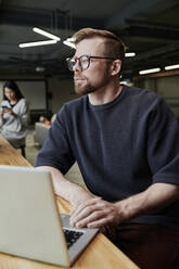 Thoughtful businessman with laptop sitting at office - DSHF00212