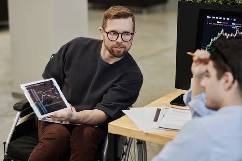 Ein behinderter Geschäftsmann zeigt einem Kollegen im Büro eine Grafik zu Kryptowährungen auf einem Tablet-PC - DSHF00227