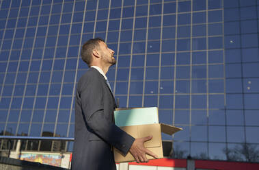 Businessman carrying box by office building on sunny day - VEGF05442