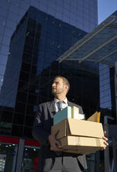 Businessman with office belongings standing in front of office building - VEGF05443