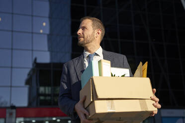 Geschäftsmann, der an einem sonnigen Tag eine Kiste mit persönlichen Gegenständen ins Büro trägt - VEGF05444