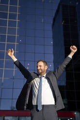 Businessman with arms raised in front of office building - VEGF05448